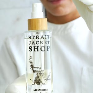 May include: A clear glass spray bottle with a bamboo cap and a white pump nozzle. The label features the black text "STRAIT JACKET SHOP" above a vintage illustration of a dental chair, with the words "MEMORIES of Dental Office" below.