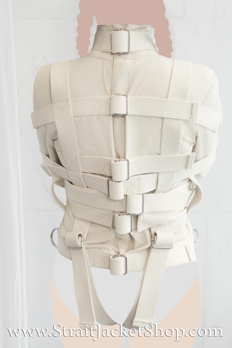 May include: A white canvas straitjacket with multiple straps and buckles. The straps are adjustable and have metal buckles. The straitjacket is designed to restrain the arms and torso. The text "www.StraitjacketShop.com" is visible at the bottom of the image.