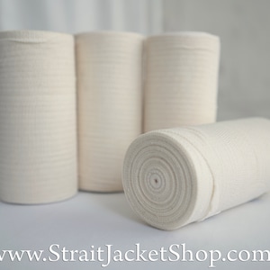 May include: Four rolls of white elastic bandage, wrapped in a spiral shape. The rolls are on a white surface.