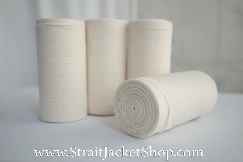 May include: Four rolls of white elastic bandage, wrapped in a spiral shape. The rolls are on a white surface.