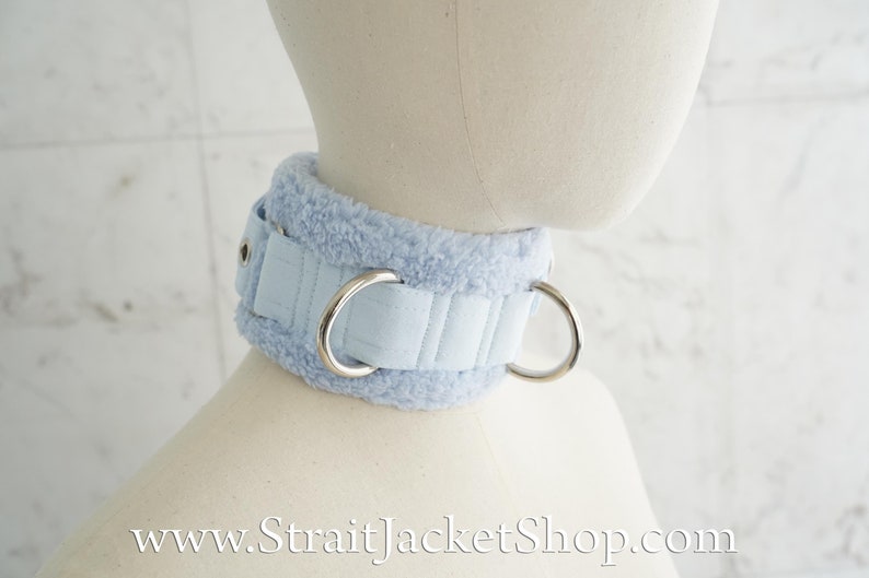 May include: A light blue faux fur choker with two silver metal rings. The choker is padded and has a stitched design. www.StraitJacketShop.com
