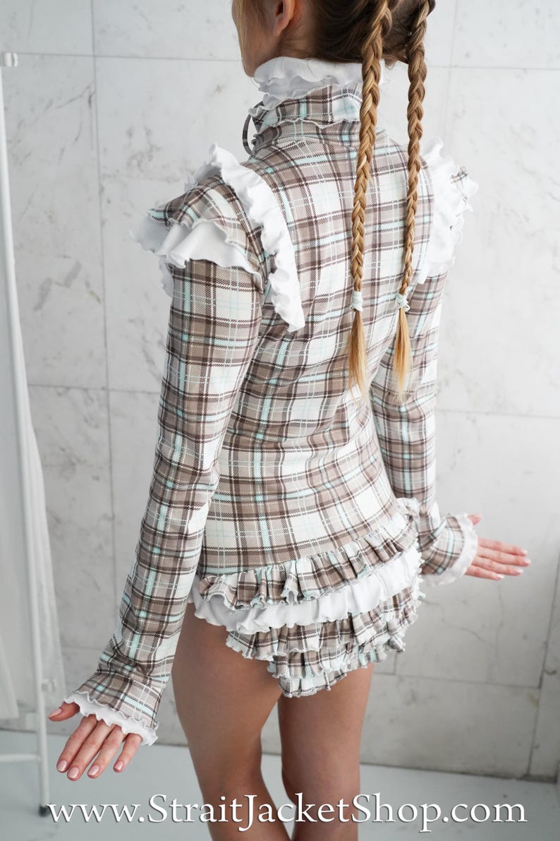 May include: A plaid top and shorts set in brown, white, and light blue. The long-sleeved top has white ruffles at the collar, shoulders, cuffs, and hem. The shorts also have white ruffles. The website address www.StraitJacketShop.com is visible.