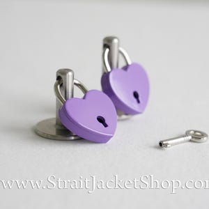 May include: Two purple heart-shaped padlocks with silver keyholes and metal rings, attached to silver bases, and a silver key.