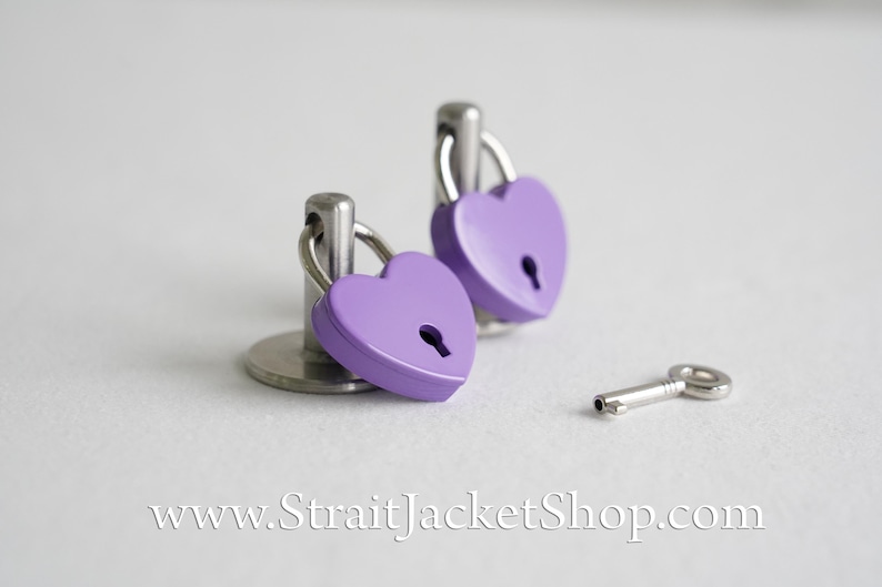 May include: Two purple heart-shaped padlocks with silver keyholes and metal rings, attached to silver bases, and a silver key.