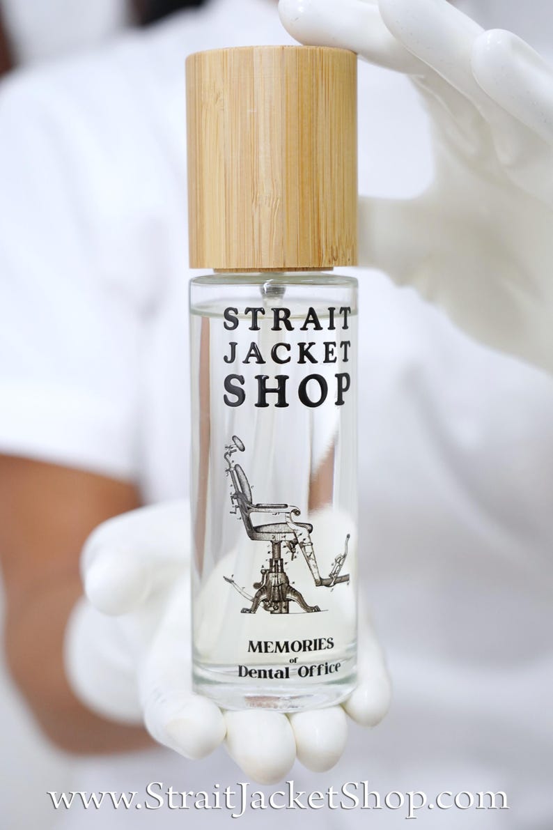 May include: A clear glass spray bottle with a light brown bamboo cap. The label features the black text "STRAIT JACKET SHOP" above a detailed illustration of a vintage dental chair, with the text "MEMORIES of Dental Office" printed below.