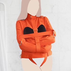 May include: A bright orange straitjacket with black straps and silver buckles. The jacket is designed to restrain the arms and torso.