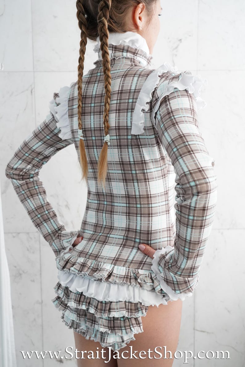 May include: A plaid long-sleeved top and shorts set in brown, white, and light blue. The top has a high collar and white ruffled trim at the shoulders and cuffs. The shorts feature multiple layers of white ruffles. The website address www.StraitJacketShop.com is visible.