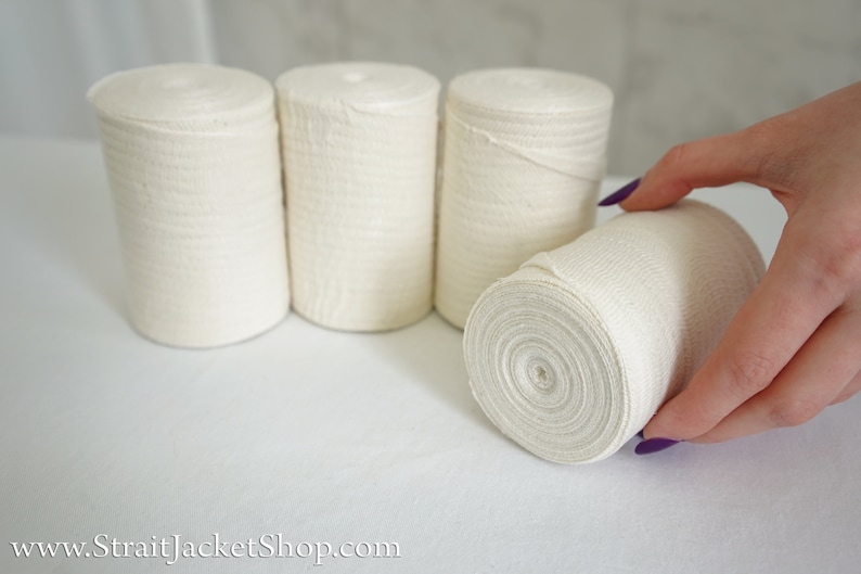 May include: Four rolls of white cotton bandage, one being held by a hand with purple nail polish.