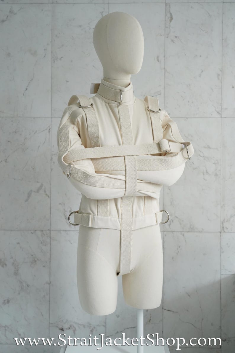 May include: A white canvas straitjacket with adjustable straps and buckles. The jacket is designed to restrain the arms and torso.