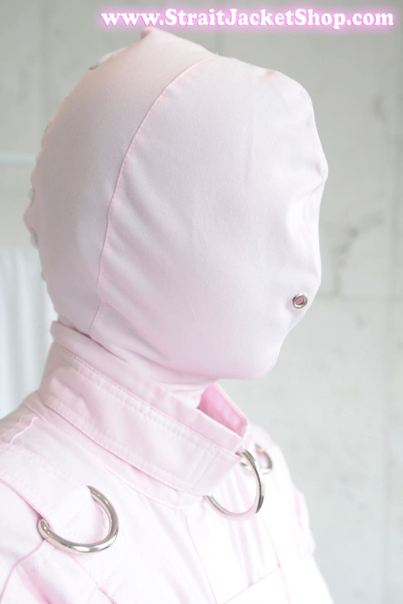 K&ouml;nnte beinhalten: Ein rosa Kapuzenkleidungsst&uuml;ck mit Rei&szlig;verschluss und zwei silbernen Metallringen an den Schultern. Die Kapuze hat eine kleine &Ouml;ffnung f&uuml;r den Mund.