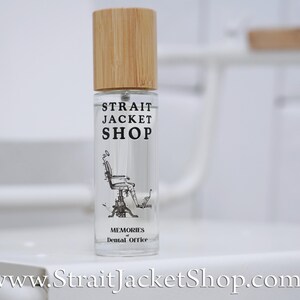 May include: A clear glass spray bottle with a light brown bamboo cap. The label features the text STRAIT JACKET SHOP, an illustration of a vintage dental chair, and the text MEMORIES of Dental Office. The website address is printed below.