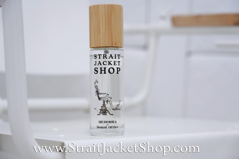 May include: A clear glass spray bottle with a light brown bamboo cap. The label features the text STRAIT JACKET SHOP, an illustration of a vintage dental chair, and the text MEMORIES of Dental Office. The website address is printed below.