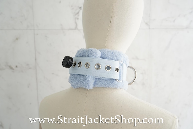 May include: A light blue faux fur choker with a silver buckle and metal eyelets. The choker has a black plastic ring on the side.
