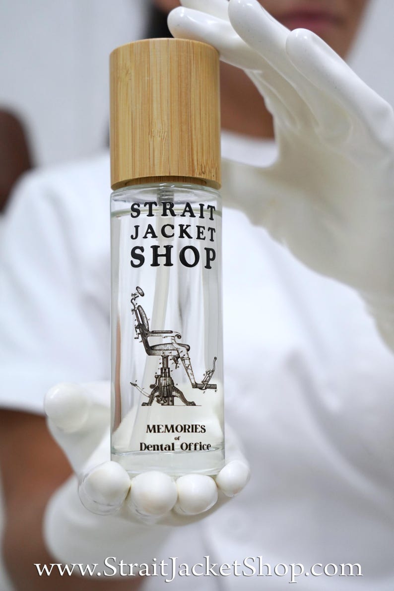 May include: A clear glass spray bottle with a light brown bamboo cap. The bottle features black text reading STRAIT JACKET SHOP and MEMORIES of Dental Office, along with a detailed black line drawing of a vintage dental chair in the centre.