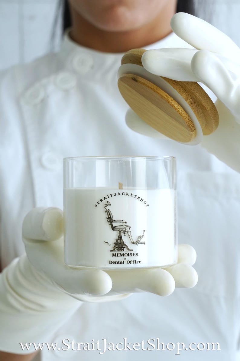 May include: A clear glass candle jar with a white wax fill and a wooden lid. The label features a black and white illustration of a dental chair with the text STRAITJACKETSHOP, MEMORIES of Dental Office, and the website StraitJacketShop.com.