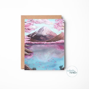 May include: A landscape painting of a mountain and lake scene. The artwork features a snow-capped mountain, pink cherry blossoms, and a lake reflecting the sky. The card is in a brown envelope with the text "calmly create".