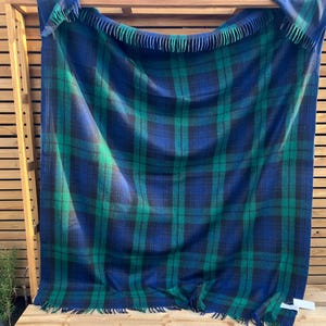 Könnte beinhalten: Eine blau, grün und schwarz karierte Decke mit Fransen an den Rändern. Die Decke ist über einer Holzkonstruktion drapiert. Das Karomuster ist ein klassisches Design mit dicken Farblinien, die ein gitterartiges Muster bilden.