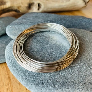May include: A stack of silver wire rings on a gray stone surface. The rings are stacked on top of each other and are all the same size.