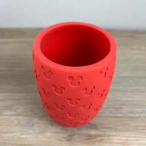 May include: A red silicone cup with a pattern of Mickey Mouse heads embossed on the outside.