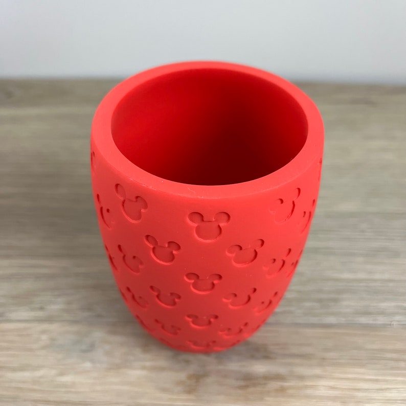 May include: A red silicone cup with a pattern of Mickey Mouse heads embossed on the outside.