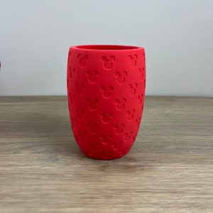 May include: A red silicone cup with a repeating pattern of Mickey Mouse heads.