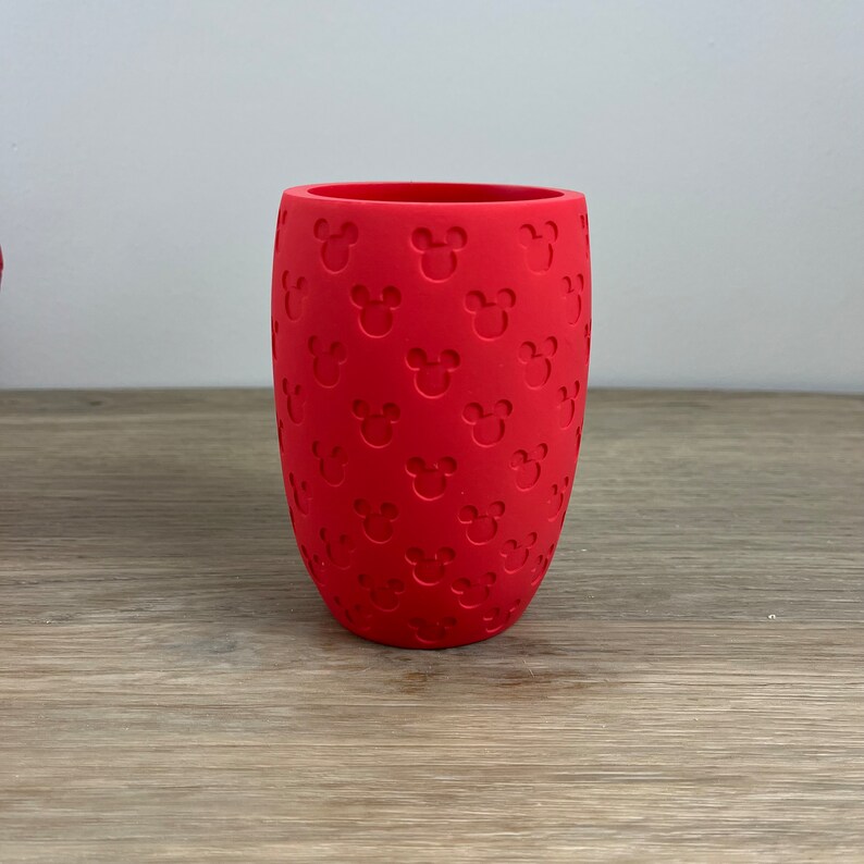 May include: A red silicone cup with a repeating pattern of Mickey Mouse heads.