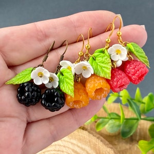 May include: Three pairs of dangle earrings featuring polymer clay fruit and flower charms. The earrings are made with gold-tone hooks and feature blackberries, raspberries, and cloudberries.
