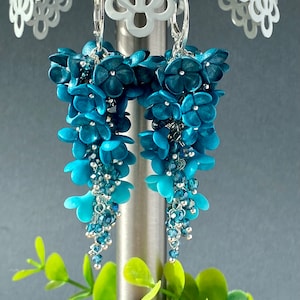 Puede incluir: Un par de pendientes colgantes con una cascada de flores de arcilla polimérica azul turquesa y cuentas de cristal.