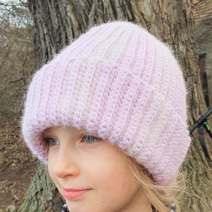 May include: A young person wearing a pink and white crocheted beanie hat. The hat has a fuzzy texture and is pulled down over their forehead.