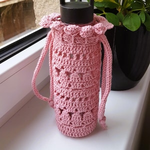 May include: A pink crocheted bottle holder with a drawstring closure and a handle. The holder is made with a delicate stitch pattern and is ideal for carrying a water bottle.