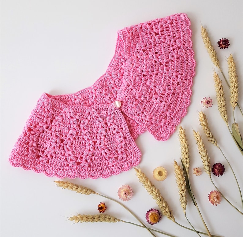 May include: A pink crocheted collar with a scalloped edge and a pearl button in the centre.