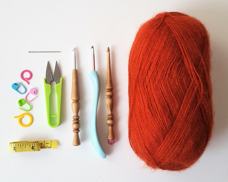 May include: A set of crochet supplies including a ball of orange yarn, two crochet hooks, a pair of scissors, stitch markers, a tapestry needle, and a measuring tape.