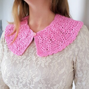 May include: A pink crocheted collar with a scalloped edge. The collar is worn over a white lace top.