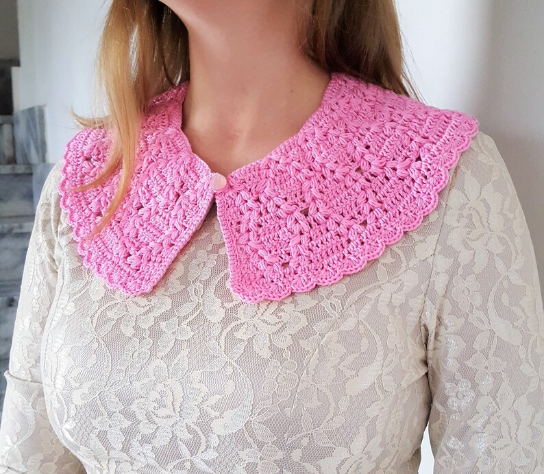May include: A pink crocheted collar with a scalloped edge. The collar is worn over a white lace top.