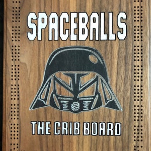 Könnte beinhalten: Ein hölzernes Cribbage-Brett mit einer dunklen Holzoptik. Das Brett zeigt ein Schwarzweißbild eines Star Wars-Charakter-Helms und den Text "Spaceballs The Crib Board".