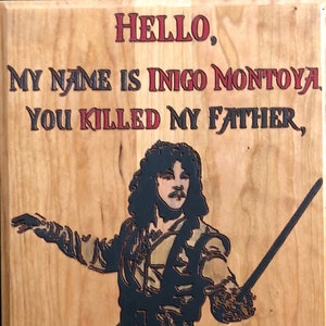 Op de afbeelding: Houten bord met een zwart silhouet van een man die een zwaard vasthoudt. Het bord heeft de tekst "HELLO, MY NAME IS INIGO MONTOYA. YOU KILLED MY FATHER, PREPARE TO DIE!" in rode en zwarte letters.