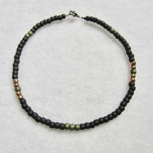 May include: A black beaded necklace with green and rose gold accents. The necklace has a silver clasp.