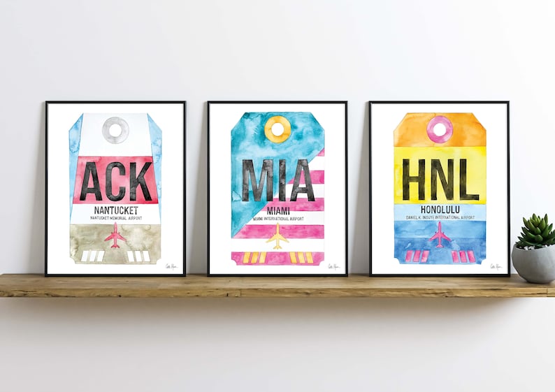 May include: Three framed watercolor prints of airport luggage tags. The tags are for Nantucket Memorial Airport (ACK), Miami International Airport (MIA), and Daniel K. Inouye International Airport (HNL).