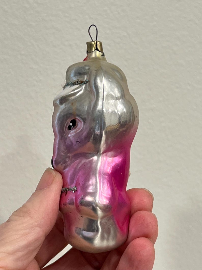 Puede incluir: Un adorno navide&ntilde;o de vidrio vintage con forma de persona con acabado rosa y plateado. El adorno tiene una cara plateada con un ojo negro y un cuerpo rosa.