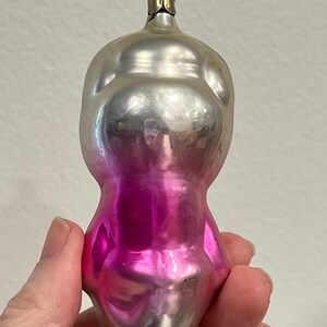Puede incluir: Un adorno navide&ntilde;o de vidrio vintage con forma de persona. El adorno es plateado en la parte superior y se desvanece a rosa en la parte inferior.