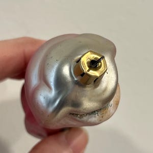 Puede incluir: Un adorno navide&ntilde;o de vidrio rosa y plateado con un colgador de metal dorado. El adorno tiene forma de campana y una superficie texturizada.