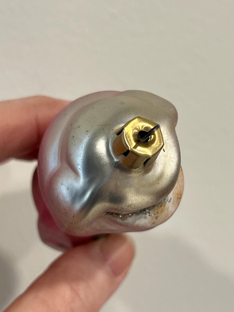 Puede incluir: Un adorno navide&ntilde;o de vidrio rosa y plateado con un colgador de metal dorado. El adorno tiene forma de campana y una superficie texturizada.