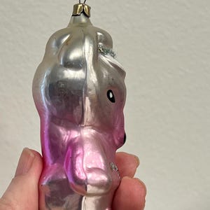 Puede incluir: Un adorno de Navidad de vidrio rosa y plateado con forma de oso con sombrero. El adorno tiene un lazo de alambre plateado para colgar.