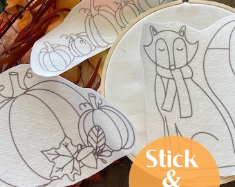 May include: Embroidery hoop with a fox design and several fabric pieces featuring pumpkin and leaf outlines. The image includes the text "Stick & Stitch" in an orange circle, suggesting a craft project or DIY kit with fall themes.
