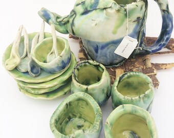 May include: A handmade ceramic tea set with a green, blue, and white glaze. The set includes a teapot, four cups, four saucers, and four spoons.