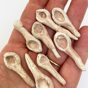 May include: A collection of ten small, hand-crafted ceramic spoons in a light brown color. The spoons have a rounded bowl and a long, thin handle.