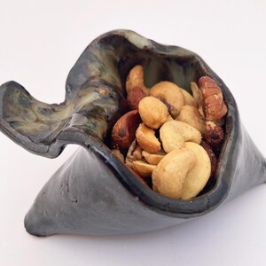 May include: A ceramic bowl with a dark green and black glaze, filled with a mix of nuts, including cashews, peanuts, and pecans.