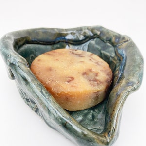 May include: A light brown bar of soap with flecks of brown and white in a blue and green ceramic soap dish.