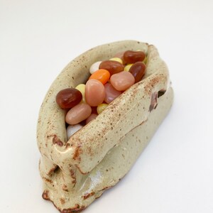 May include: A ceramic dish shaped like a boat filled with colorful jelly beans. The dish is a light beige color with brown speckles.
