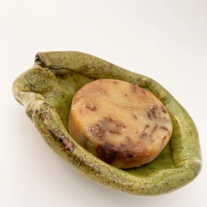 May include: A green ceramic soap dish shaped like a hand holding a bar of brown soap.